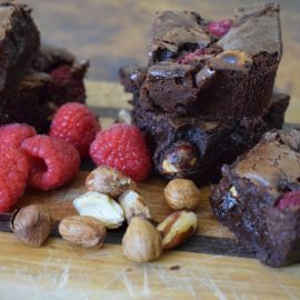 Scrumptious raspberry and cobnut brownies on wooden board surrounded by cobnuts
